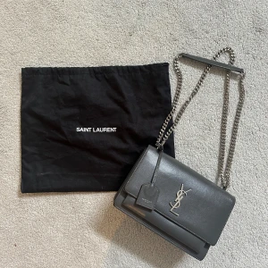 Ysl väska  - Säljer min fina limited edition väska från Saint Laurant (grå/silver). Köptes hösten 2020 på nk i Göteborg (kvitto finns). Modell: Sunset Medium. Nypris: 24 181 kr. Skickar självklart fler bilder vid efterfrågan. 😊