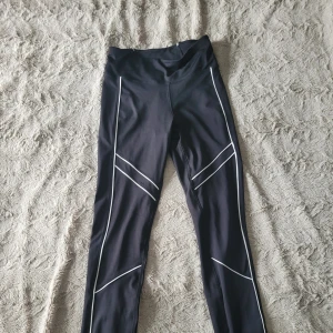 Strongertights med vita linjer - Svarta träningstights från Stronger med vita linjer. Använt max 2 gånger. Snygga, lite unika men ändå också lite basic. Funkar till mycket. Liten ficka baktill. Nypris 899. Anons nr. 14.