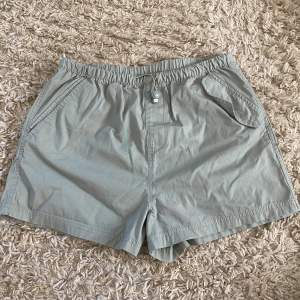 Ett par grön gråa  shorts från märket Divided. Shortsen har en elastisk midja och en knapp framtill. De har två fickor fram och en ficka bak.