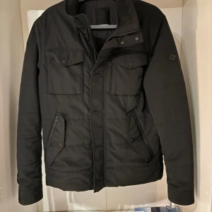J.Lindberg fieldjacket - Väldigt fin J.Lindberg fieldjacket i svart färg, skick 9/10, köpt på J.Lindbergs hemsida för 2,700kr, mitt pris kan diskuteras! 