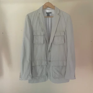 Beige kavaj från Filippa K - Filippa K- En beige/offwhite safari-jacka/kavaj. i linne och bomull.  Den är rejäl men ändå avslappnad men funkar bäst på våren, den tidiga hösten och många svenska sommarkvällar. Material: 80% bomull, 20% linne. Storlek50/Large. Mått- Längd: 83cm Axlar: 46cm Byst: 52cm Midja 46cm Ärm: 47cm -Skick: Använd på ett fint och respektfullt sätt. 