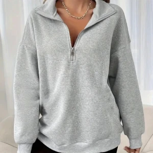 Grå sweatshirt med dragkedja - En helt ny oanvänd sweatshirt med dragkedja framtill. Tröjan har långa ärmar och en hög krage som kan justeras med dragkedjan. Perfekt för vardagsbruk och kyligare dagar.