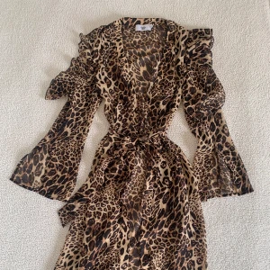 Rebecca Stella kimono i leopardmönster - Supersnygg kimono i leopardmönster med volanger från Rebecca Stella. Använd endast en gång, i nyskick, utan anmärkningar. Cut-out vid armen/axeln och knyts i midjan med band.