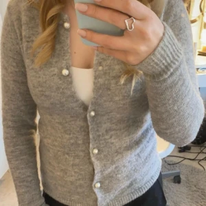 Grå stickad kofta - En superfin grå stickad kofta med vita pärlknappar. Fint skick och är strechig i materialet. 