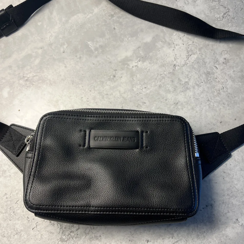 Snygg axelväska/waistbag från Calvin Klein. Knappt använd, nypris 899kr. Mått: H14cm, L21cm & B7cm. Väskor.