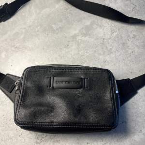 Snygg axelväska/waistbag från Calvin Klein. Knappt använd, nypris 899kr. Mått: H14cm, L21cm & B7cm