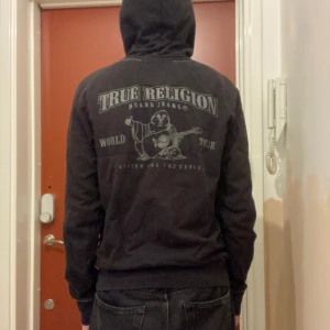 True Religion zip hoodie - True Religion hoodie med ett snyggt tryck på ryggen. Storlek S (passar M) i herrstorlek men snygg på båda könen. Den är köpt i USA och är svår att hitta i Sverige. En knapp vid fickan saknas men annars har den inga defekter. Hör av dig vid fundering.