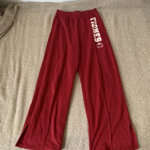 Röda mjukisbyxor från H&M - Ett par röda mjukisbyxor från H&M med texten 'TIGNES' tryckt på vänster ben. Byxorna har en elastisk midja och slitsar vid bensluten.