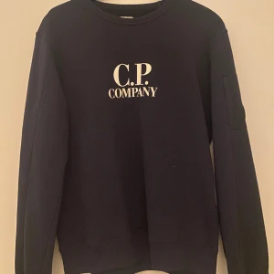 Cp company tröja  - En jättefin sparsamt använd cp company tröja. Den är äkta lappen finns kvar, köpt på KidsBrandStor. Den är i S den passar även XS. Passar dam och herr. Den har en liten ficka på armen med trycket. Fler bilder kan skickas. Frakt ingår ej