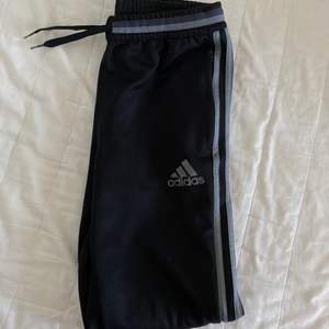 Svarta Adidasbyxor med grå ränder och dragkedja vid vaderna som säljs då de inte kommer till användning.
