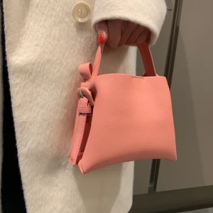 Mini väska från Mango - Supersöt rosa mini väska från mango, men rymmer ändå det som behövs! Har använt den 2 gånger så ser helt ny ut! Går att bära i handen samt på Axel/över kroppen