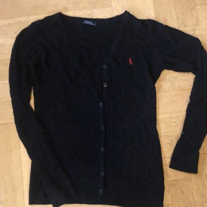 Ralph Lauren kofta S - Svarat ribbad kofta med knappar och Ralph Lauren märket vid bröstet på vänster sida. Jag har köpt den second hand men det är väldigt bra skick. Både snygg att ha knäppt och uppknäppt. Tvättas innan den skickas.