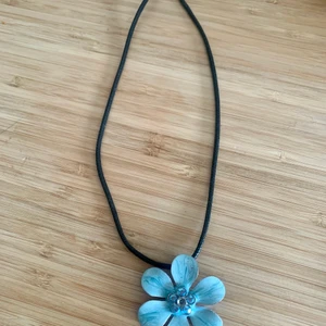 Blommigt halsband - Ett vackert halsband med en statement blomma. Blomman är fäst på ett band av glansigt rep. Perfekt för att pigga upp en outfit!