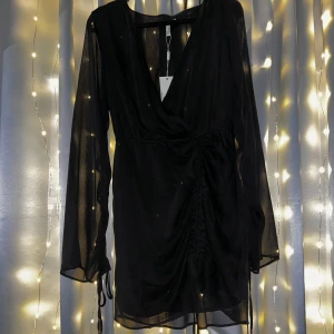 Svart klänning från Nelly - Köptes för 3 månader sedan men har tyvärr inte kommit till användning. En fin svart klänning med snören man kan justera ärmarnas längs. Detta finns även på kjolen. Jättefin till utetillfällen med kompisar! 