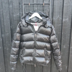 Moncler Maya Jacka - Säljer nu min svarta Moncler Maya Jacka, i storlek M. För mer bilder eller fråga skriv bara. Köpt av en nära vän och vet inte om den är äkta eller inte ( tror inte den är äkta dock )  Inga fel på jackan förutom ett jätte litet hål i fickan.