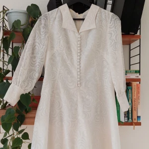 Studentklänning - Vit klänning i 60/70-tals stil. See through i ärmarna. Klänningen är i mini modell och går till ca halva låret. Den är skön att ha på sig och har fina detaljer med knappar. 