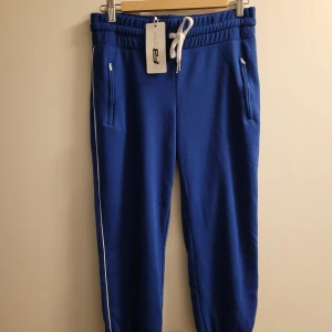 Trekvartsbyxa i tyg - Trekvartsbyxa i mjukistyg med dragkedja på vardera sida. Oanvända med lappar kvar. 