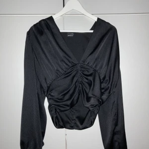 Svart kort topp med knappar i  - Jätte snygg och glansig topp (svårt å få till på bild) med knappar i kortare modell i storlek 40, men skulle snarare säga att den passar 36-38. Fler bilder kan fås vid önskemål :) 
