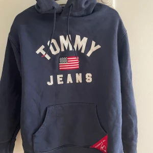 Tommy Jeans Hoodie - Tjock Hoodie, för en avslappnad stil. Varm och Mysig. Använts till att gå promenad och  utflykter. Använt relativt sällan. Köt för 1100 kr.