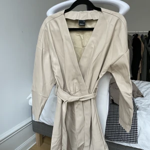 Ny PU klänning  - Helt ny beige klänning i läderliknande (PU) material, Går omlott med ett bälte i midjan.  Storlek 36