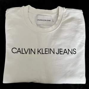 Vit collegetröja från Calvin Klein Jeans i storlek S. Tröjan är använd ett par gånger och är i väldigt fint skick. 