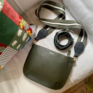 Grön Axelremsväska Whyred  - Grön axelremsväska i skinn och mocka från Whyred. Två axelremmar medföljer. Den randiga är köpt på Lindex och den smala i skinn är original till väskan. Ca 23 x 17 cm stor. Fint begagnat skick enligt bild. 