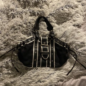 Handväska - Svart handväska med silverdetaljer. Har ett stort fack och ett mindre med dragkedja. Nitar på utsidan. 