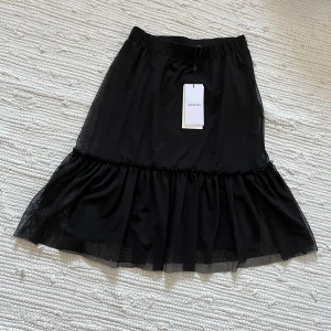 Svart kjol - Svart kjol i två lager, en underkjol och en övre del i tunt lite genomskinligt material. Helt oanvänd med prislappen kvar. Längd 57 cm. Midja (med stretchig resår) 63cm