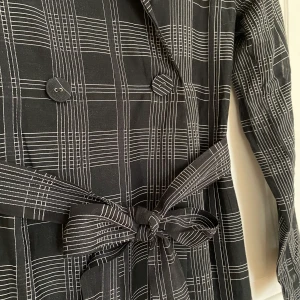 Anna dress från Whyred storlek 34 - Väldigt fin klänning från Whyred. Den är dubbelknäppt upptill och har bälte i midjan.  Ärmarna är i mer genomskinligt tyg än resten av klänningen. Fint fall. Skickar spårbart. 