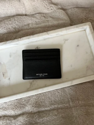 Korthållare - Säljer denna superfina korthållare från Michael Kors. Mycket klassisk och stilren design i svart skinn och logga i silver. Sparsamt använd. Köpt för 500kr.