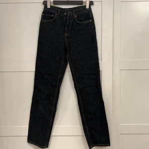 Svarta jeans - ASOS DESIGN mid rise '90's' straight leg jeans in vintage washed black. Använda 2-3 gånger och har inga skador, men passar tyvärr inte mig längre. Fem ficksmodell med knappar framtill och kopparfärgade sömmar.