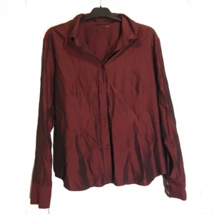 burgundy skjorta - Mörkröd/burgundy skimrande skjorta i polyester. Köpt second hand men i fint skick, inte använd mycket av mig. Passar antagligen xs-m beroende på hur man vill att den ska sitta, längdmässigt sitter den bra på mig som är 168 cm.