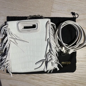 Maje väska - Säljer denna vita maje väska. Väskan är köpt på NK för 2700kr. Till väskan tillkommer en guldig kedja som passar perfekt att ha över axeln, och även ett längre vitt band som är justerbart . Väskan har lite missfärgning vid handtaget, Inget man tänker på.