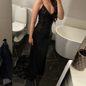 Svart lång klänning - Svart lång klänning i paljetter. Med ett kortare släp. Stl XS- S. Jag är 165 cm lång och klänningen nuddar precis golvet framför mina fötter. Jag köpte den till balen men använde den aldrig, så den är oanvänd. Axelbanden är justerbara. Super fint skick. 