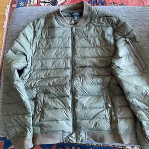 Polo Ralp Lauren - Kakigrön lättviktsdunjacka med muddar på armarna och längst ner. Ficka finns på vänstra armen. Normal passform.