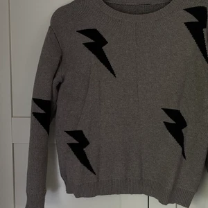 Stickad tröja med blixtrar! - Stickad tröja i storlek S! Använd endast 1 gång. Bra kvalitet, grå med svarta blixtrar.