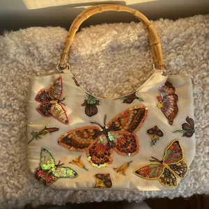 Väska med fjärilsmotiv - Så fin o unik handväska md fjärilsmotiv! Ena sidan har paljetter och pärl-brodering. Kan stängas med dragkedja samt har en ficka inuti. Köpt i en vintage butik i London så ser lite använd ut. Se tredje bilden för storleksreferns mot en MacBook Air.