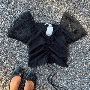 Svart, kort topp i spetsmaterial med puffärm.  - Svart, kort topp i spetsmaterial med puffärm från H&M med prislappen kvar.  Stl M. 