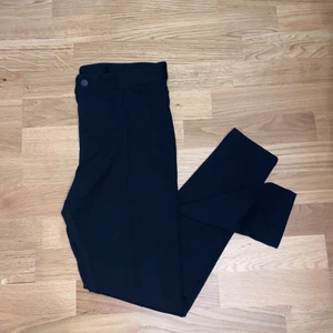 Svarta byxor - Tightsliknande byxor med söm längs framsidan av benen och knäppning i midjan. Aldrig använda. Strl M.