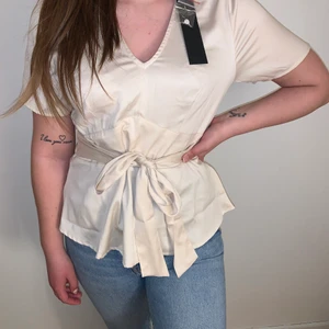Champagne färgad blus - Helt ny och oanvänd blus med knyte i midjan med en liten v-ringad urringning. 