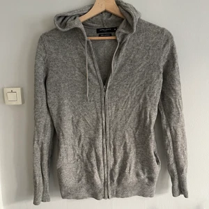Grå kashmir hoodie - Jättefin ljusgrå kashmirhoodie med zip från Galeries Lafayette, storlek 00 som motsvarar xs. Ett litet lagat hål vid en av fickorna på framsidan därav priset. 100% cashmere, snygg söm på mitten av ryggen baksidan, något figursydd.