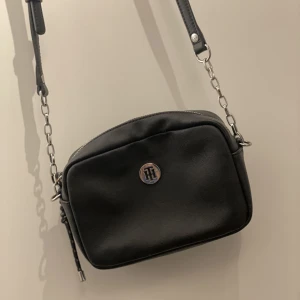 Tommy Hilfiger | Äkta - En Tommy Hilfiger handväska i gott skick. Har använt den ett fåtal gånger. Den är svart med coola detaljer. 