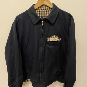 Sällsynt harrington jacka Aquascutum - Reversible vintage harrington jacka från brittiska märket Aquascutum. Mörkblå på ena sidan och beige och mörkblå rutor på andra. Toppen skick, inga flaws. Inköpt från  brittiska toohotlimited.com Taggad M men sitter som en lite oversized M eller kort L. 