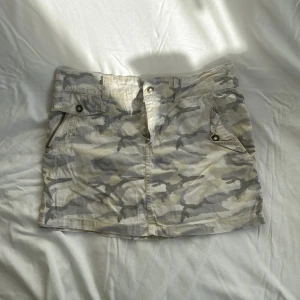 Low waist mini kjol Y2K  - Så snygg y2k minikjol i militärmönster med broderier och diamant knappar. Längd 33 cm, midja ca 37 cm rakt över. Dragkedjan funkar inte och den har en väldigt liten fläck (bild 3), därav priset. Köps via Swish eller köp nu 💋 