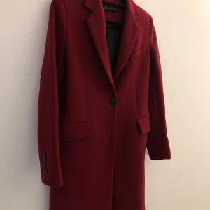 Kappa Zara ull - Vinröd ullkappa från Zara i ull/ullblandning. Smickrande färg och modell, något figursydd. Supersnygg nu på hösten! Är använd men i jättefint skick. Finns två knapphål men jag har tagit bort ena knappen, finns kvar och kan enkelt sys på om man vill. Strl XS men passar även S. Ev. Frakt tillkommer