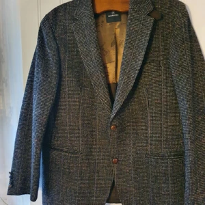 Tweedkavaj Mönster Brun/Grå Storlek L/XL - Skräddarsydd, brun/grå tweedkavaj (herr) med läderknappar. Rutmönstrad med vita, svarta och bruna trådar. 100% ull och handvävd.