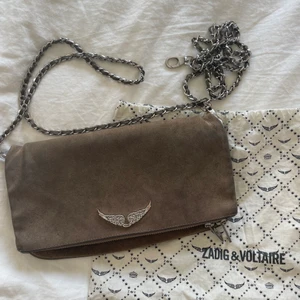 Zadig&Voltaire väska  - Rock Suede Clutch i färgen taupe. Använd flitigt och i helt ok skick. Dustbag och båda kedjorna följer med. 