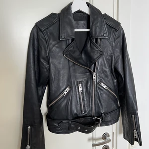 Skinnjacka från AllSaints - Skinnjacka ifrån AllSaints i en rak ”bikermodell”. Jag köpte den för ca 2,5 år sedan på NK (kvitto medföljer) men senaste året bara har den hängt i garderoben, därav dags att sälja vidare. Den är sparsamt använd och är i fint skick.