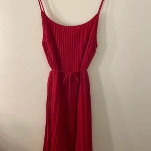 Röd långklänning - Klänningen är i storlek S och är ungefär till knäna. Den går att knyta i midjan och skapar en fin siluett. Klänningen är i ett lyxigt material och kan användas på lite finare tillställningar.