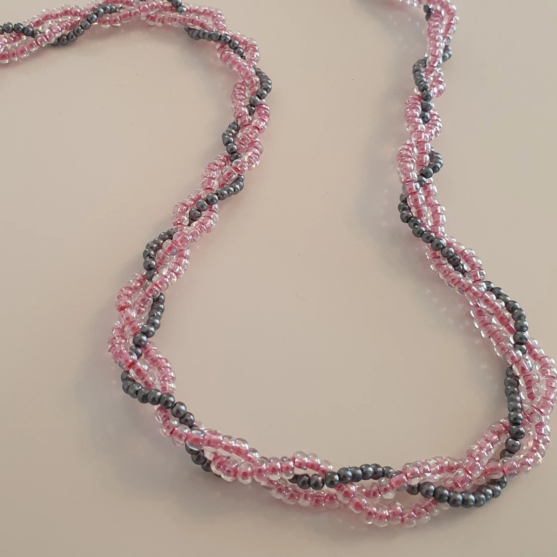Ett flätat pärlhalsband i rosa och grått. - 91